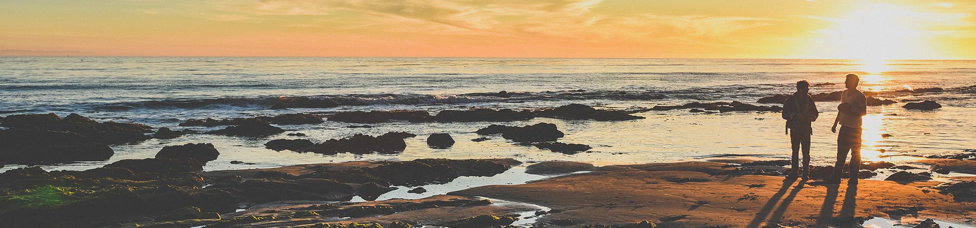 Two friends standing on the beach foreshore with sunset.